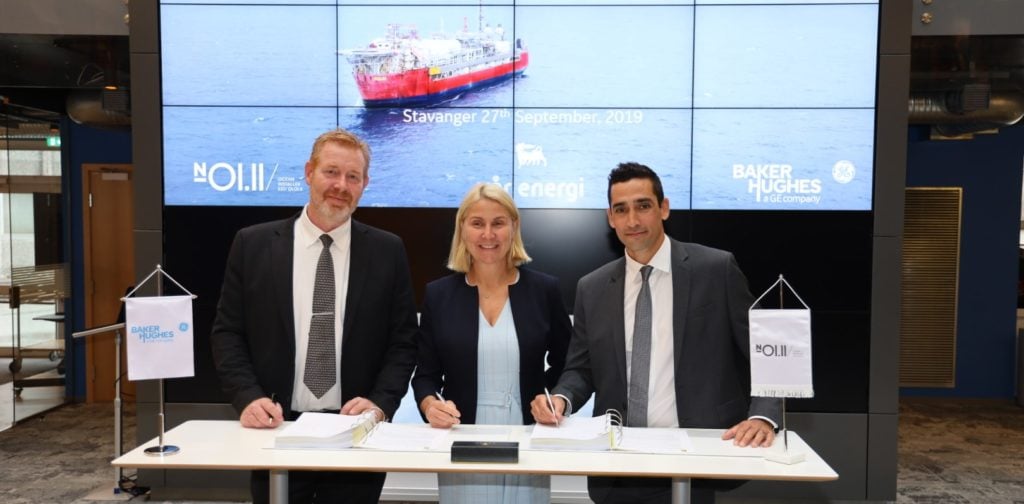 Three people standing at a table signing av contract. Photo.