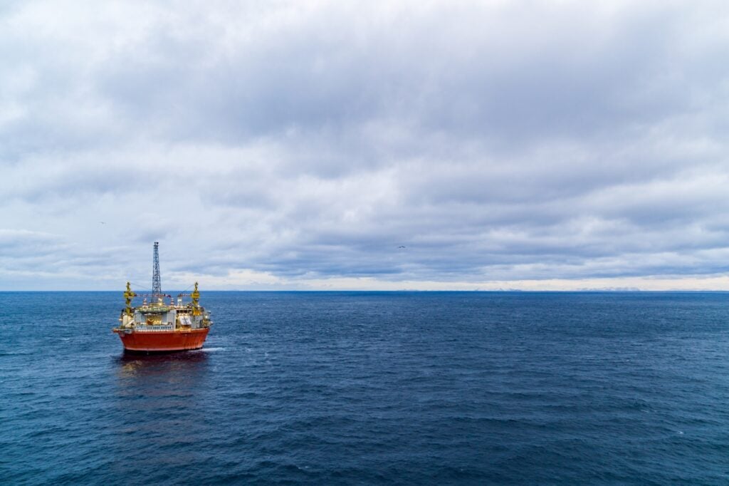 Oil platform in calm sea. Cloudy sky. Mountains in a distance. Photo.