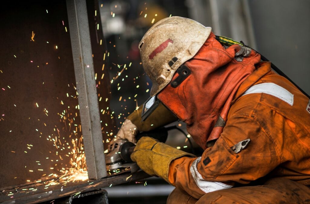 Worker in orange coverall. Sparks from a grinder. Photo.