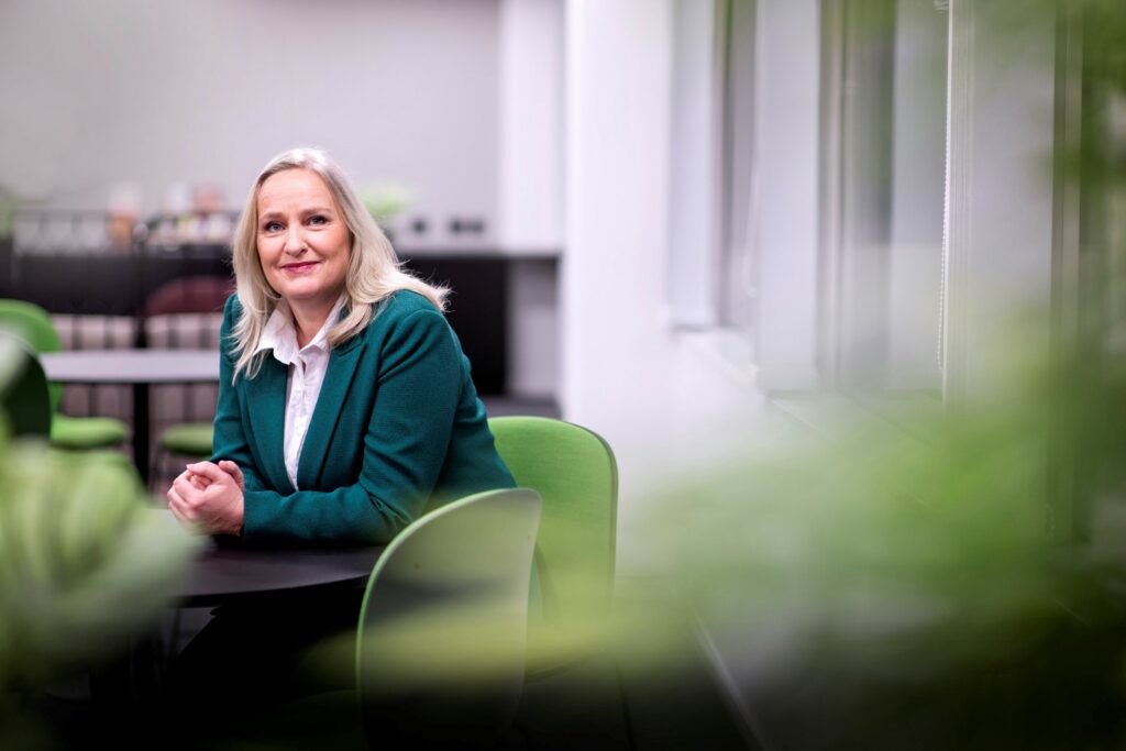 Tone Rognstad sitting on a green chair at a brown table. Photo.